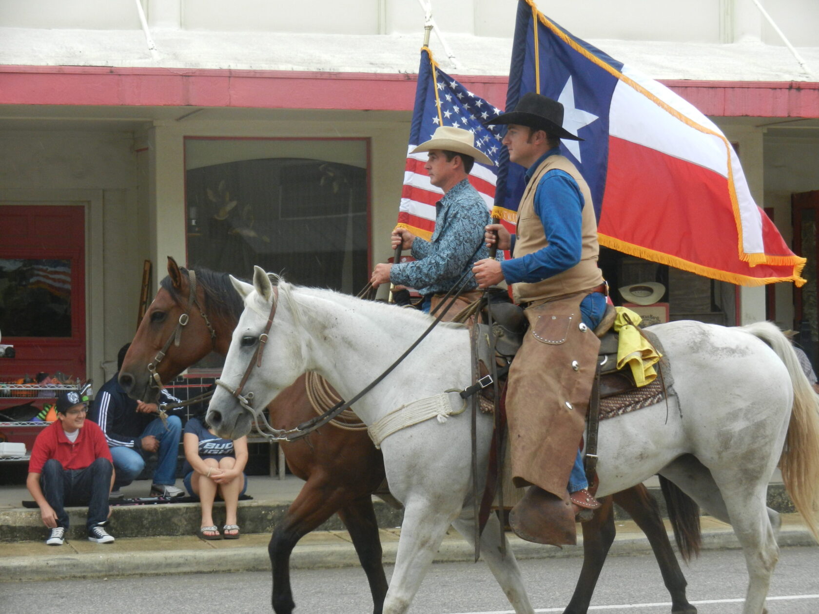 Two men riding horses down a street with flags.